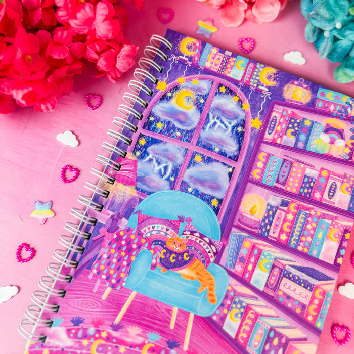 A spiral-bound notebook with a whimsical purple and blue library illustration, styled on a pink background with colorful flowers and decorative stickers.