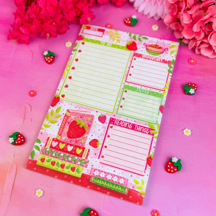 Notepad with strawberry design on a pink background with flowers and decorative items.