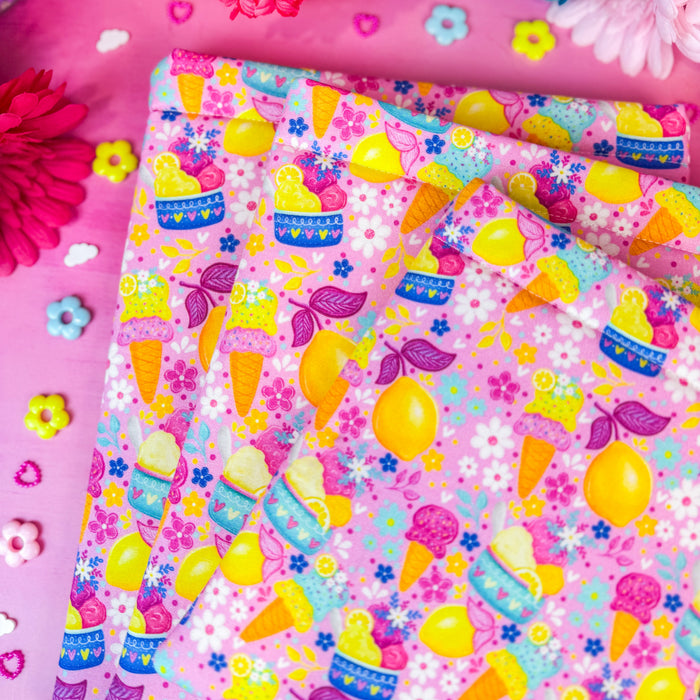Three book sleeves with a colorful ice cream cone and lemon pattern, styled on a pink surface with flowers and decorative elements.