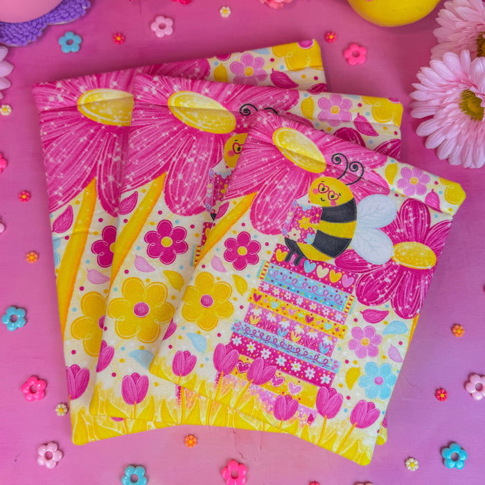 Colorful book sleeves with cartoon bee design on a pink background with flowers.