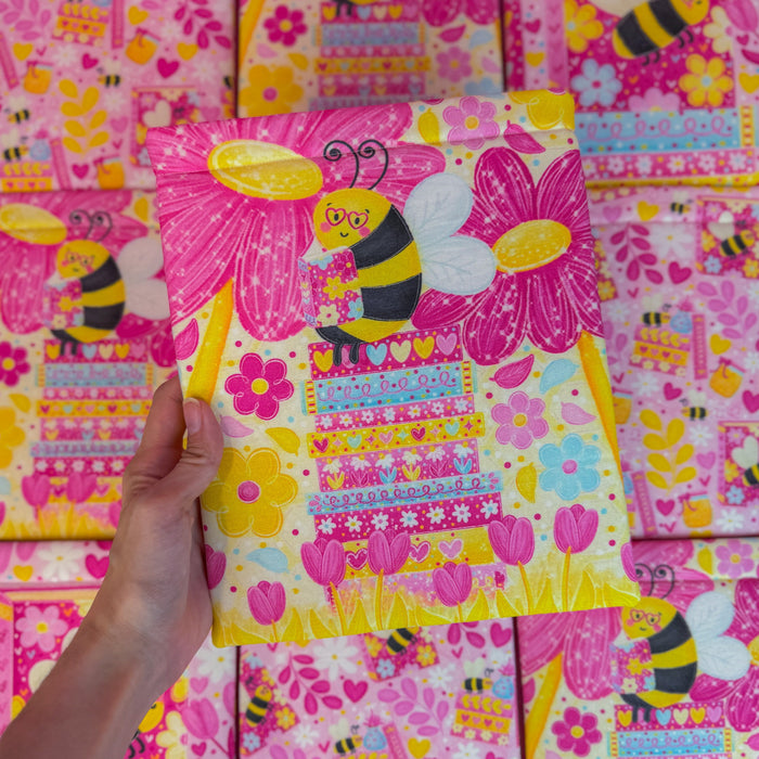 Colorful fabric with bee and flower patterns, held by a hand against a matching fabric background.