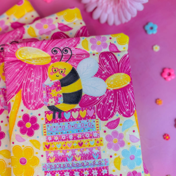 Colorful book sleeve with a bee design on a pink background with flowers.