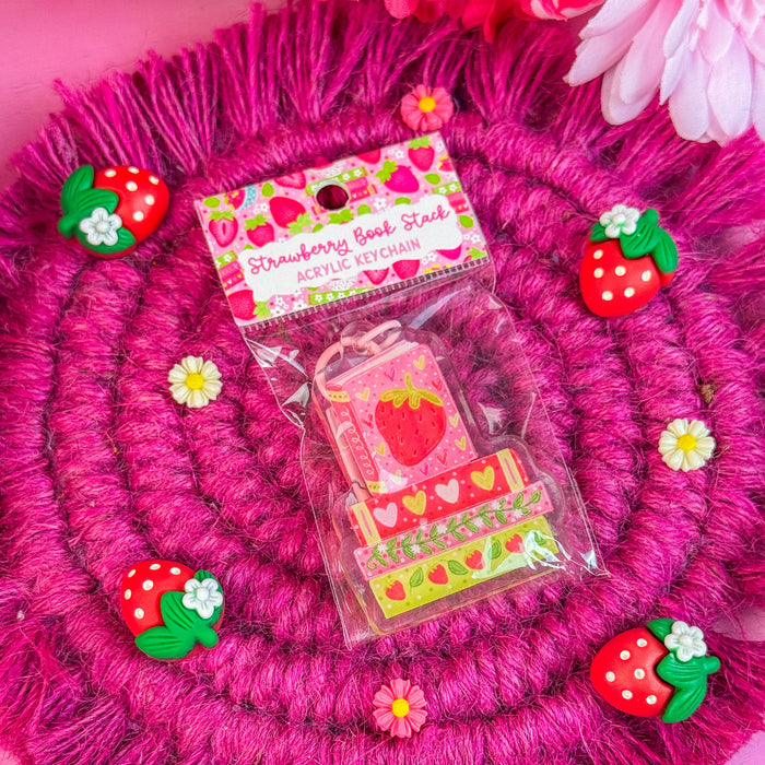 Strawberry-themed keychain on a pink textured surface with flowers in the background