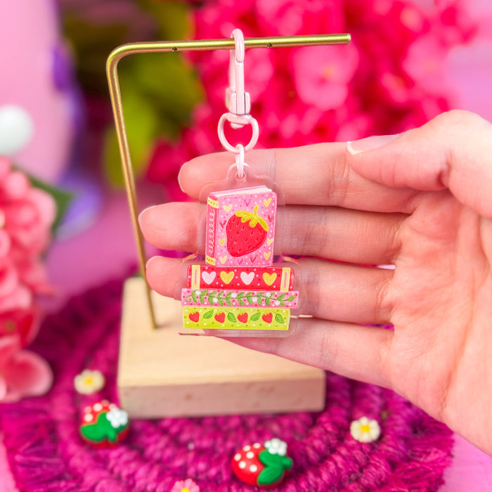 Hand holding a colorful strawberry-themed keychain with a blurred floral background