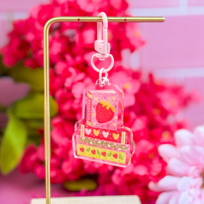Decorative stand with a strawberry book stack keychain against a pink floral background