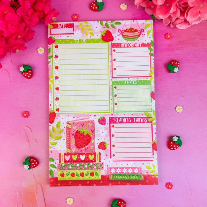 Colorful notepad with strawberry design on a pink background with flowers and decorative items.
