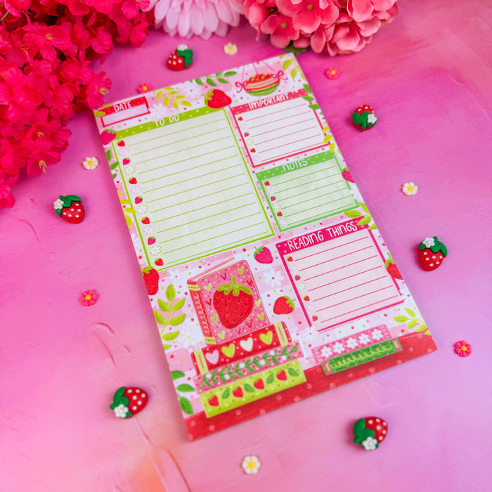 Colorful notepad with strawberry design on a pink background with flowers and decorative items.