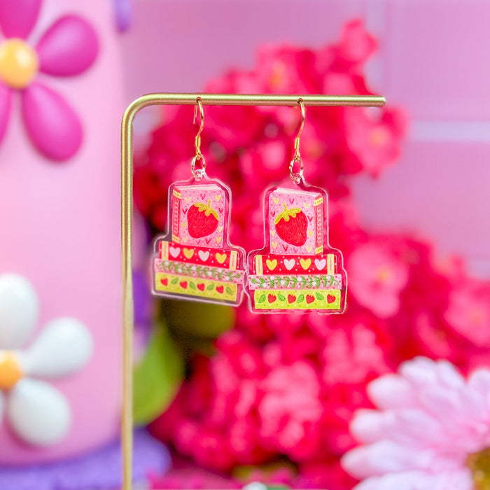 Colorful earrings on a stand with a pink floral background