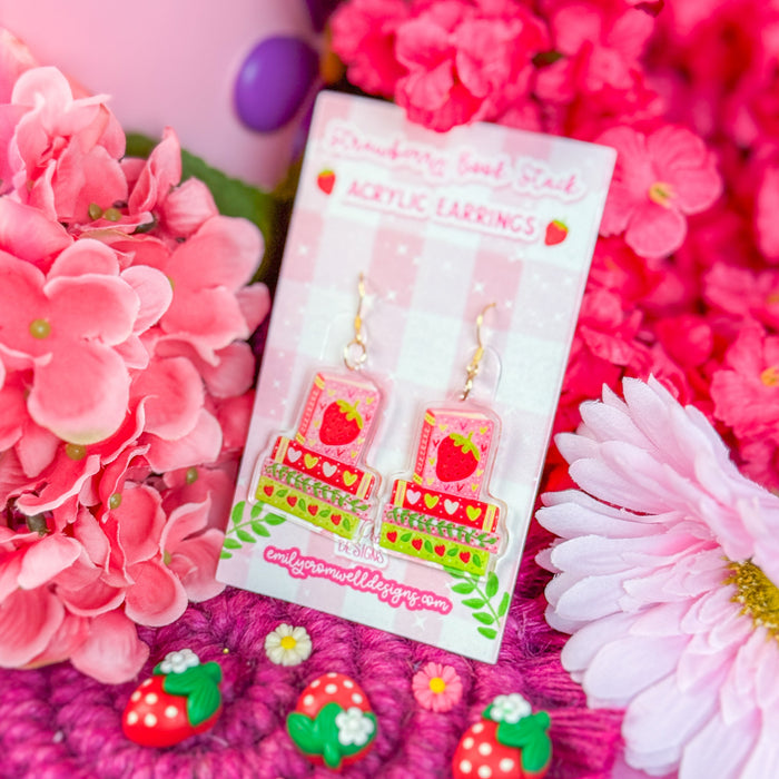 Strawberry-themed earrings in packaging with pink flowers and a pink background