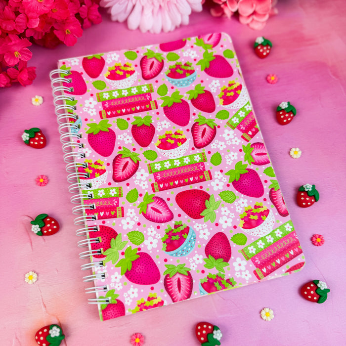 Notebook with strawberry pattern on a pink background with flowers and decorative items.