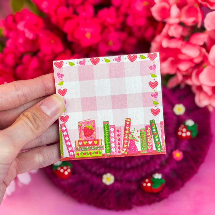 Hand holding strawberry-themed sticky notes against a pink floral background