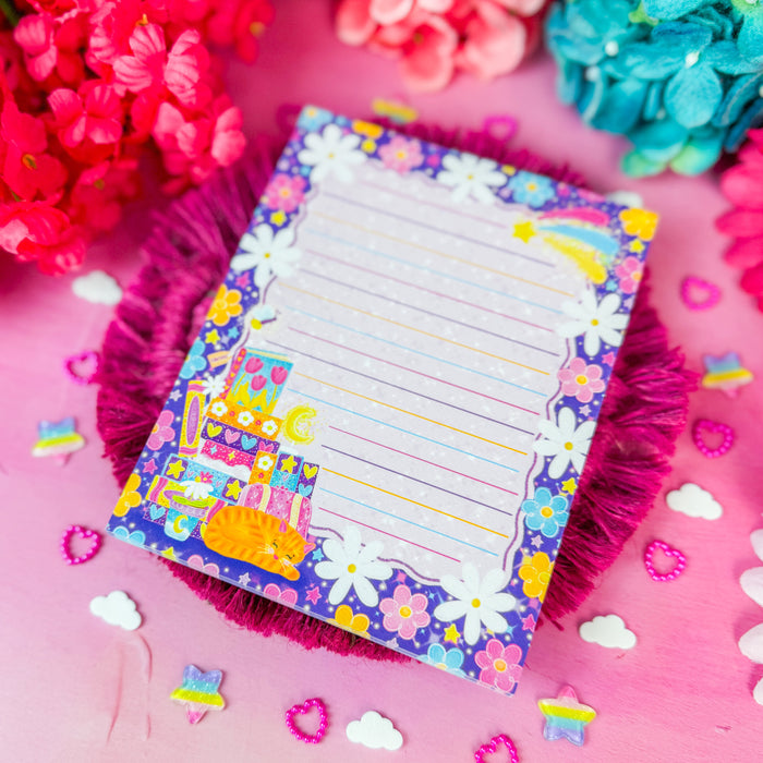 A colorful lined notepad with a floral border and cartoon character, styled on a pink surface with bright flowers and small decorative accents.